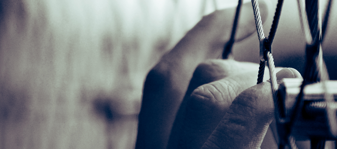 image of a hand with fingers clinging to a fence the person is trapped behind